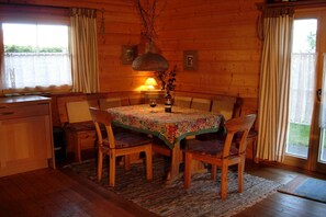 A wooden cabin interior with a dining table, chairs, a hanging light fixture, and a window with curtains. - Holiday home in Zingst with barbecue (Zingst)