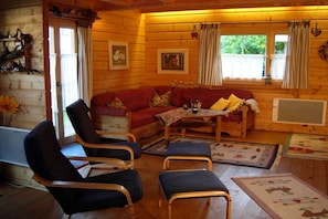 Un acogedor interior de cabaña con una pared de troncos de madera, un sofá rojo, dos sillones, una mesita y un televisor.