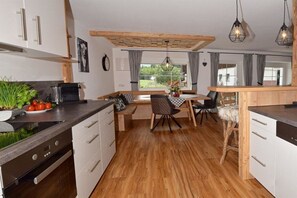 A modern kitchen with wooden flooring, white cabinetry, a dining area with a bench, and pendant lighting. - Holiday apartment with 1 bedroom (Immenstadt-Bräunlings)