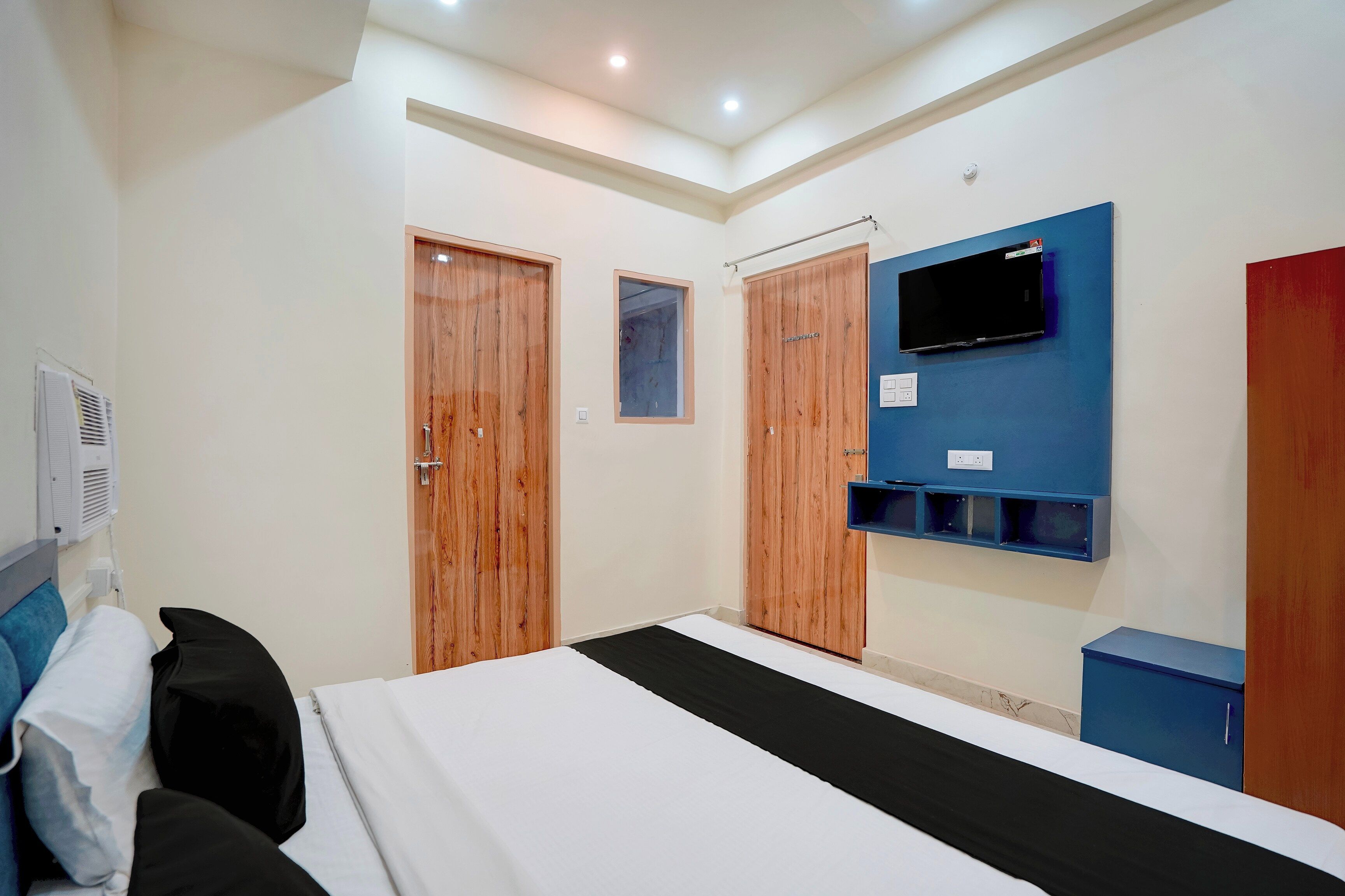 A hotel room with a bed, a TV mounted on the wall, wooden wardrobes, and a window.