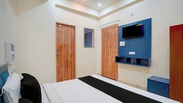 A hotel room with a bed, a TV mounted on the wall, wooden wardrobes, and a window.