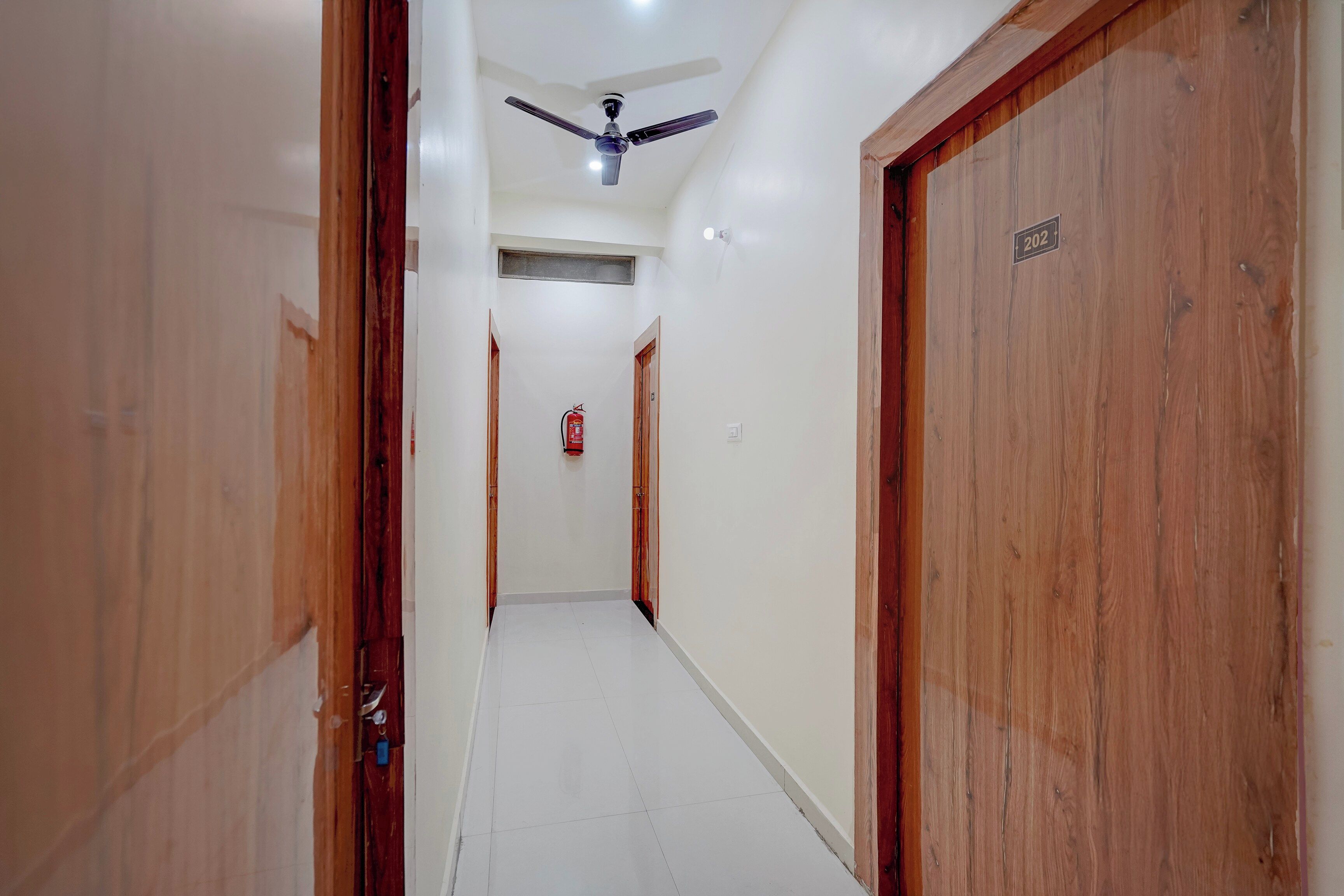 A hallway with wooden doors, a ceiling fan, and a fire extinguisher on the wall.