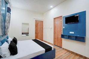 Un dormitorio con una cama, un televisor montado en la pared, una puerta de madera y un espejo.