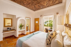 Ein Schlafzimmer mit einem großen Bett, Holzboden, einem Badezimmer mit Dusche und Blick auf Grün.