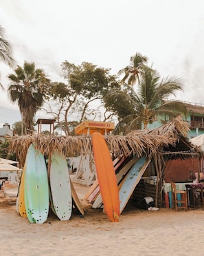 Escena de playa con tablas de surf apoyadas en una estructura de paja.