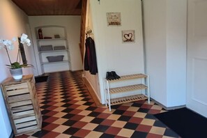 Ein Flur mit einem Schachbrettmuster-Boden, einer hölzernen Bank mit Topfpflanze, einem Kleiderständer und einem Schuhregal.