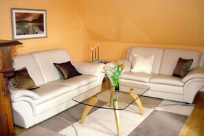 A living room with a glass coffee table, two sofas, a framed picture on the wall, and a vase with flowers on the table. - Bella Rosa **** Lüneburg (Lüneburg)