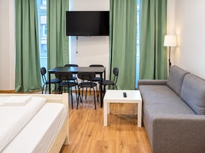 A hotel room with a bed, a sofa, a dining table with chairs, a TV mounted on the wall, and a lamp. - Palace Days and Concert Nights 2BR near Westbahnhof (Vienna)