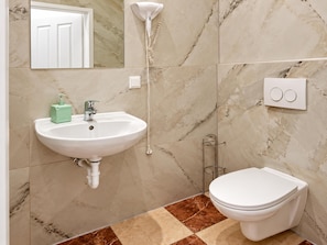 Een badkamer met een wit wastafelmeubel, een toilet en een douchekop aan de muur.