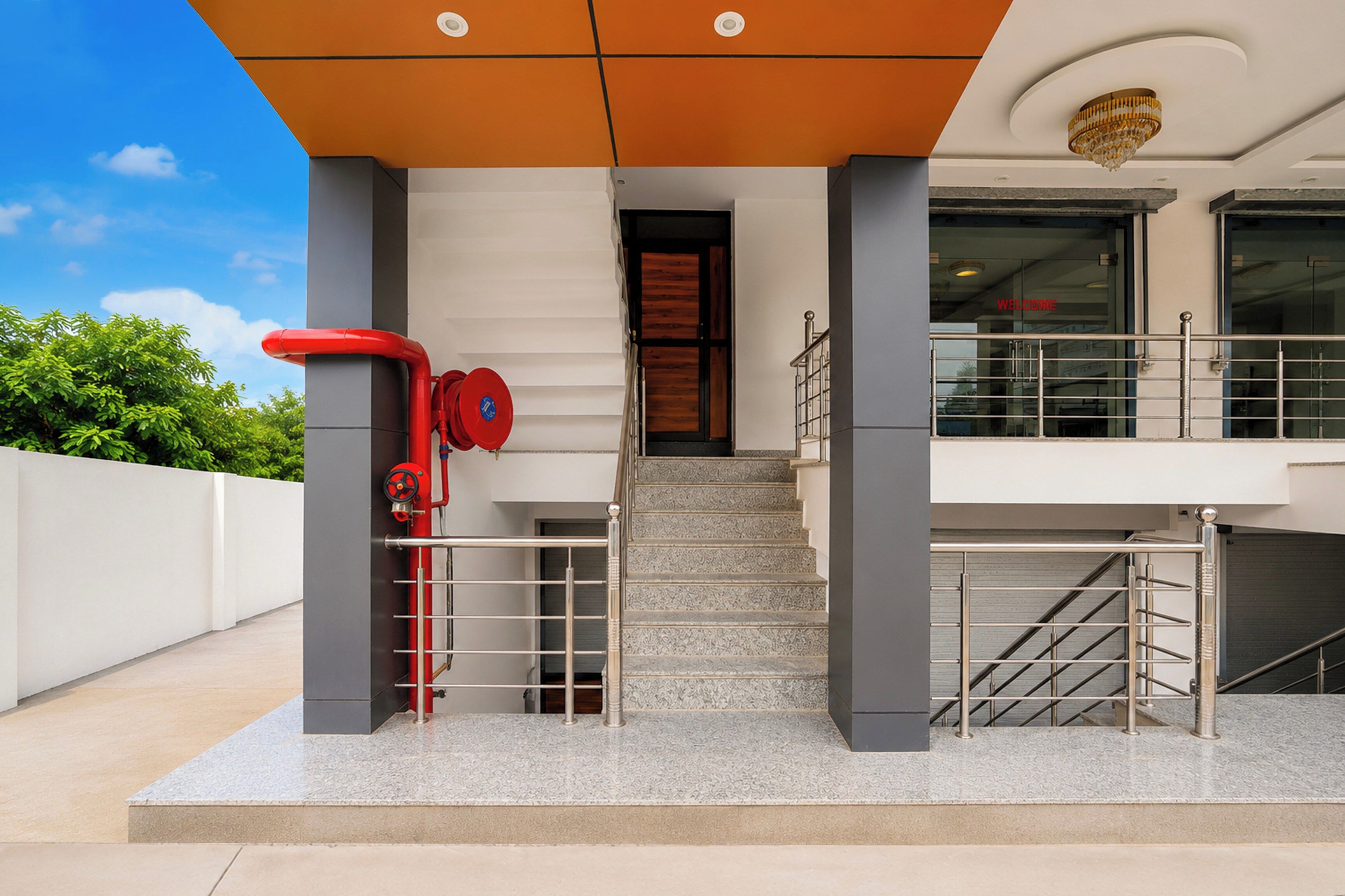 A building entrance with a staircase leading to a second floor, a red fire hose, and a metal railing.