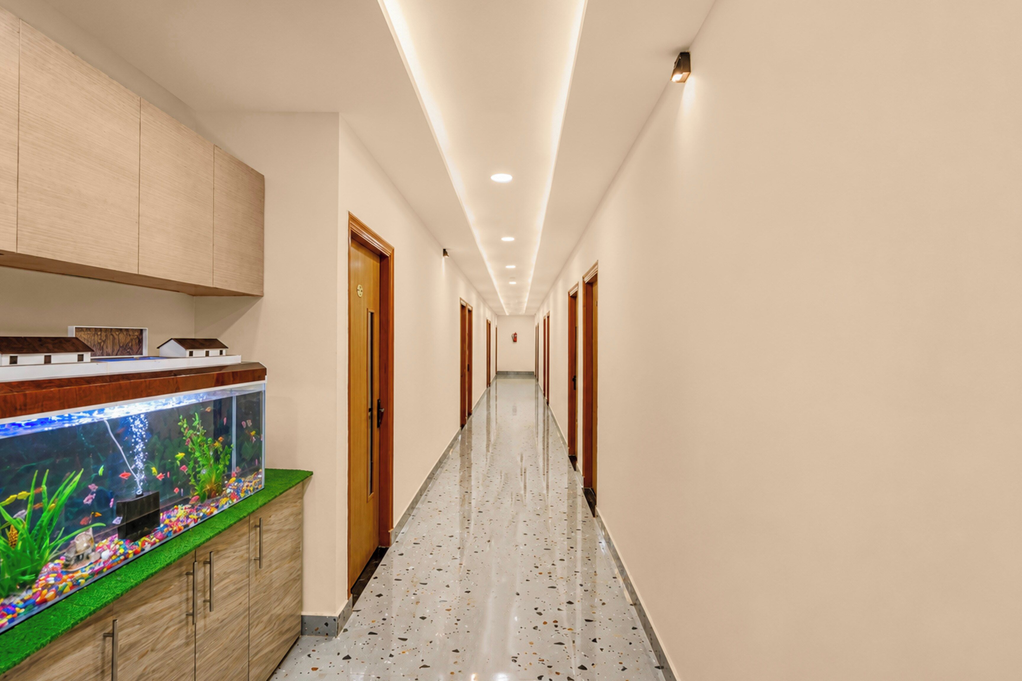 A hallway with a fish tank, wooden cabinets, and a speckled floor.