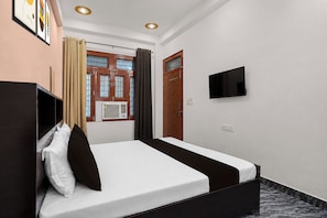 Una habitación de hotel con una cama, un televisor montado en la pared y un ventanal con cortinas.