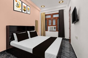 Una habitación de hotel con cama, televisión, ventana con cortinas y cuadros en la pared.
