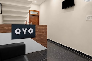 Un comptoir d’accueil avec une enseigne indiquant « OYO », situé dans le hall d’un hôtel moderne, avec un escalier et un téléviseur à écran plat fixé au mur.
