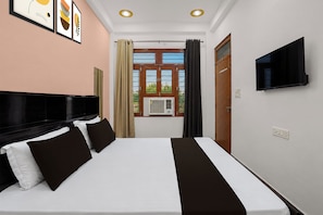 Habitación de hotel con cama, televisión de pantalla plana, ventana con cortinas e aire acondicionado de pared.