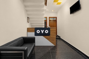 Un área de recepción con mostrador, un sofá de cuero negro, una escalera y una puerta de madera.