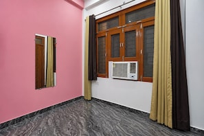 Une pièce aux murs roses, une fenêtre ornée de rideaux bruns, un climatiseur blanc et un sol à motifs de marbre.