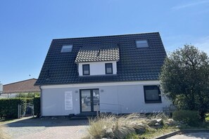Ein modernes, zweistöckiges Gebäude mit dunklem Dach, einem kleinen Balkon im Obergeschoss und einem verschlossenen Eingang.