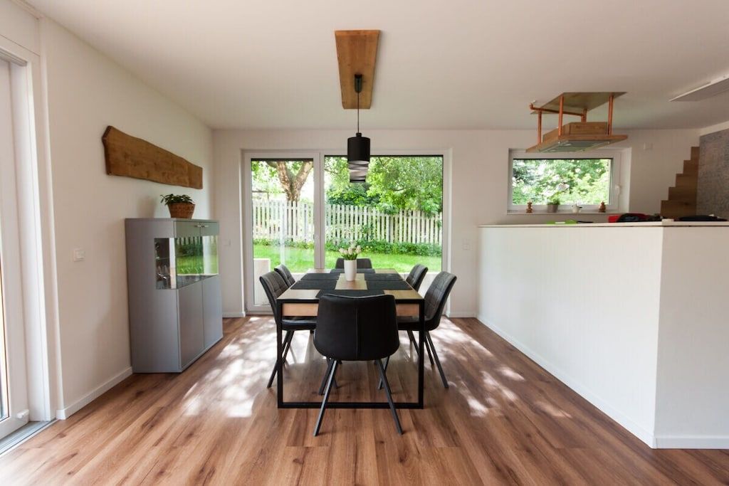 A modern kitchen with a dining area, wooden flooring, and a view of the outdoors.