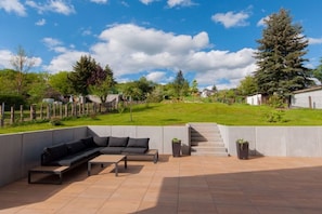 An outdoor patio area with a sofa and coffee table, surrounded by a low wall and a grassy lawn. - Holiday home South Harz (Neustadt\/Harz)