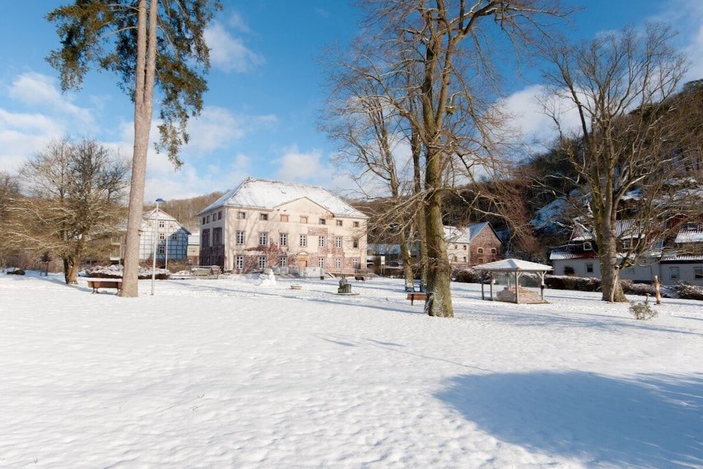 Ein verschneiter Park mit einem großen Gebäude, Bänken und Bäumen.