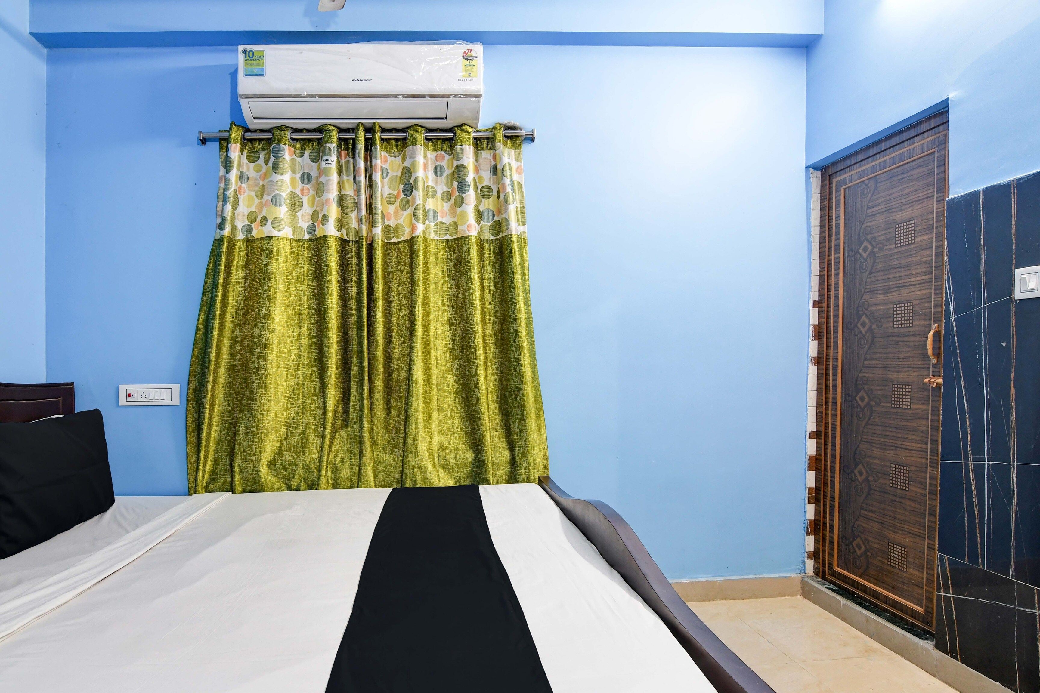 Un dormitorio con cama, ventana con cortinas, unidad de aire acondicionado y puerta.