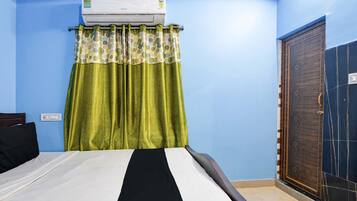 Un dormitorio con cama, ventana con cortinas, unidad de aire acondicionado y puerta.