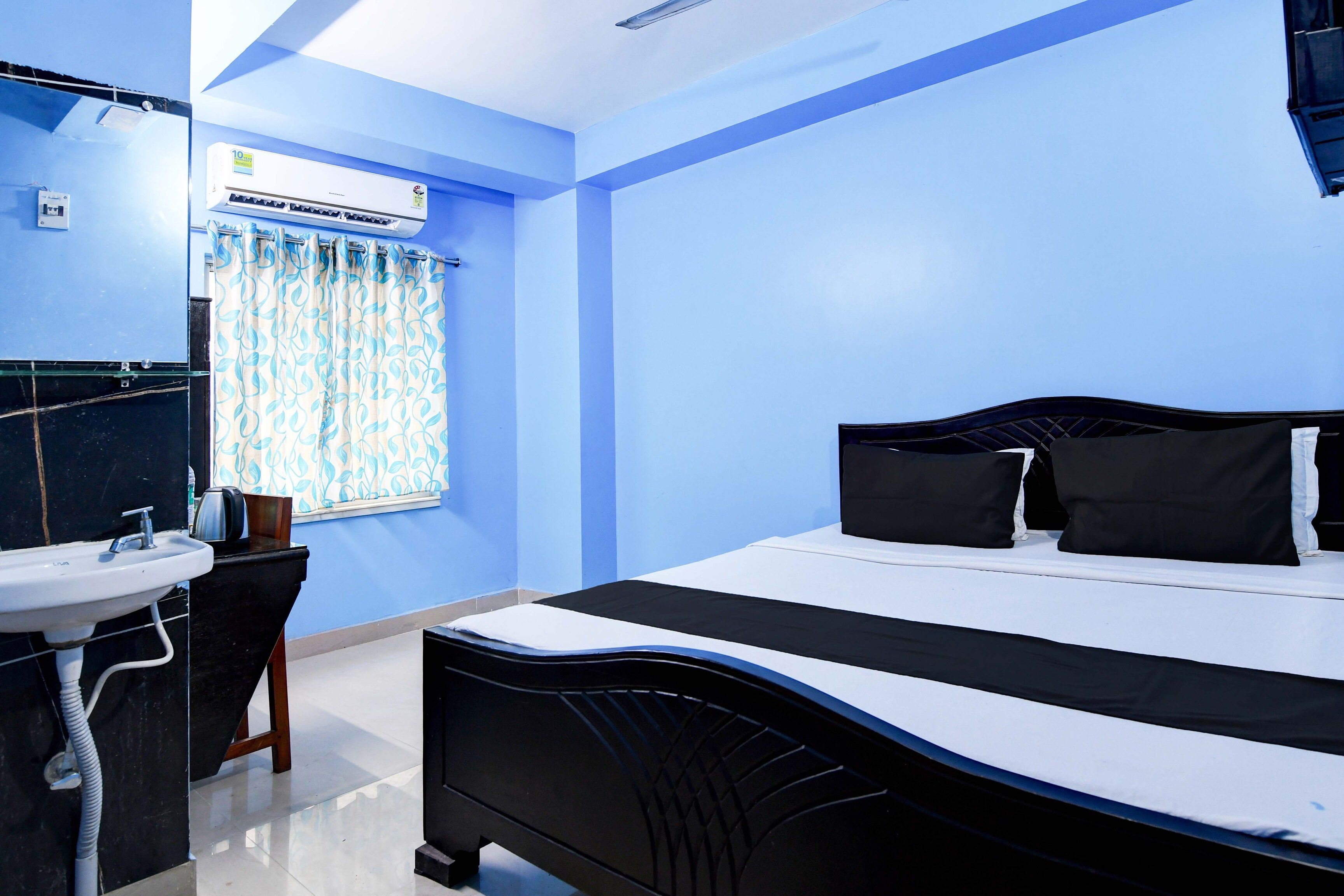 Habitación de hotel con cama, mesita de noche, espejo, ventana con cortinas, lavamanos y aire acondicionado de pared.