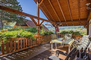A covered outdoor seating area with a table and chairs, surrounded by a wooden fence and lush greenery. - Holiday apartment with 1 bedroom (Oberkirch-Bottenau)