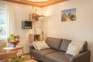 A living room with a brown leather sofa, a small table with a vase of flowers, and a floor lamp. - Holiday apartment with 1 bedroom (Oberkirch-Bottenau)