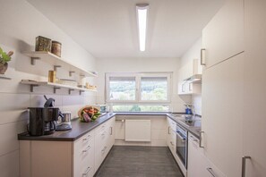 A modern kitchen with white cabinetry, a built-in oven, and a window providing a view of the outdoors. - Holiday apartment with 1 bedroom (Oberkirch-Bottenau)