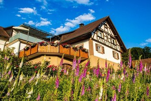A traditional half-timbered house with a balcony, surrounded by vibrant flowers. - Holiday apartment with 1 bedroom (Oberkirch-Bottenau)