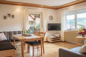 Een gezellige woonkamer met een bank, een eettafel met stoelen, een televisie en een raam met uitzicht.