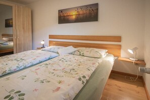A bedroom with a wooden headboard, a bed with floral bedding, bedside lamps, and a wall-mounted painting. - Holiday apartment with 1 bedroom (Oberkirch-Bottenau)