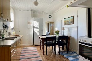 A kitchen with wooden cabinets, a refrigerator, a dining table with chairs, and a stove. - Holiday home in Tenhult with swimming pool (Tenhult)