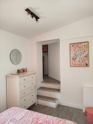 Ein Schlafzimmer mit Bett, Kommode, Spiegel und einem gerahmten Poster an der Wand.