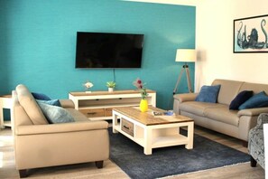 Ein Wohnzimmer mit Sofa, Couchtisch und Fernseher an einer türkisfarbenen Wand.