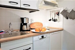 Een keuken met een spoelbak, koffiezetapparaat en een schaal fruit.