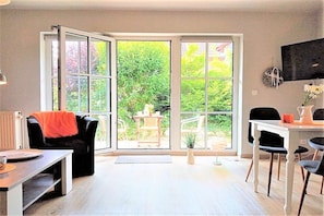 A room with a sliding glass door leading to a garden, a dining area with a table and chairs, and a sofa with a blanket. - Holiday apartment with 2 bedrooms (Schönhagen)