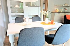 A dining area with a white table, grey upholstered chairs, a white pitcher, and a candle on a yellow coaster. - Holiday apartment with 2 bedrooms (Schönhagen)