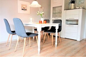 Een eethoek met een witte tafel en stoelen, een hanglamp en een kast met glazen deuren.