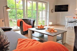A living room with a sofa, a table with a plate of fruit, a chair, and a TV mounted on the wall. - Holiday apartment with 2 bedrooms (Schönhagen)