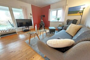A living room with a sofa, a television, a fireplace, and a window with curtains. - Holiday home in Geel with swimming pool (Geel)