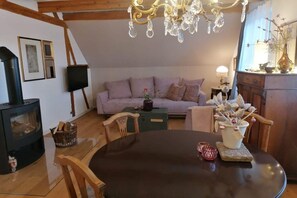 A cozy living room with a fireplace, a sofa, a dining table, and a chandelier. - Small Courtyard - Rose Red (Endingen)