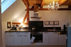 A kitchen with a black countertop, white cabinets, a stainless steel range hood, a chandelier, and a skylight. - Small Courtyard - Rose Red (Endingen)