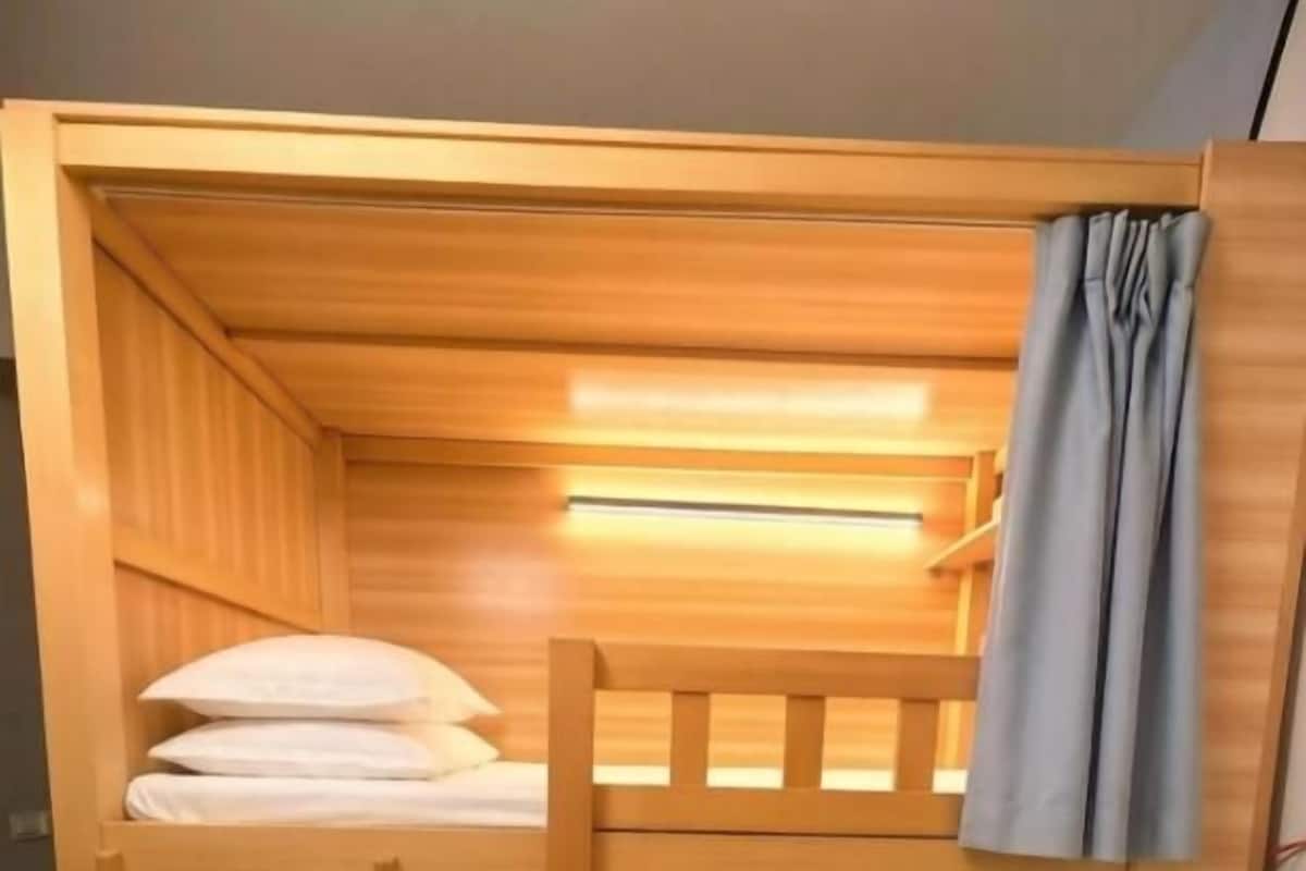 Una cama litera con estructura de madera, una plaza inferior con escalera y una superior con almohadas.