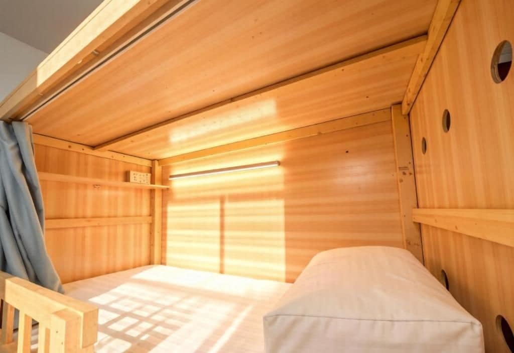A wooden cabin with a single bed, a window with blinds, and a small shelf.