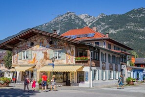 A building with a mural, a shop on the ground floor, and a mountain backdrop. - Holiday apartment Ariane (Garmisch-Partenkirchen)