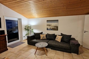A living room with a dark grey sofa, a round coffee table, and a wooden ceiling. - Holiday apartment Ariane (Garmisch-Partenkirchen)