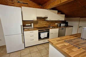 A compact kitchen with white cabinets, a wooden countertop, a built-in oven, and a stainless steel sink. - Holiday apartment Ariane (Garmisch-Partenkirchen)